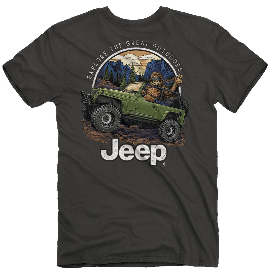 a deep gray t-shirt with an illustration of a sasquatch driving a jeep and flashing a peace sign with the jeep logo and the text “explore the great outdoors” around it