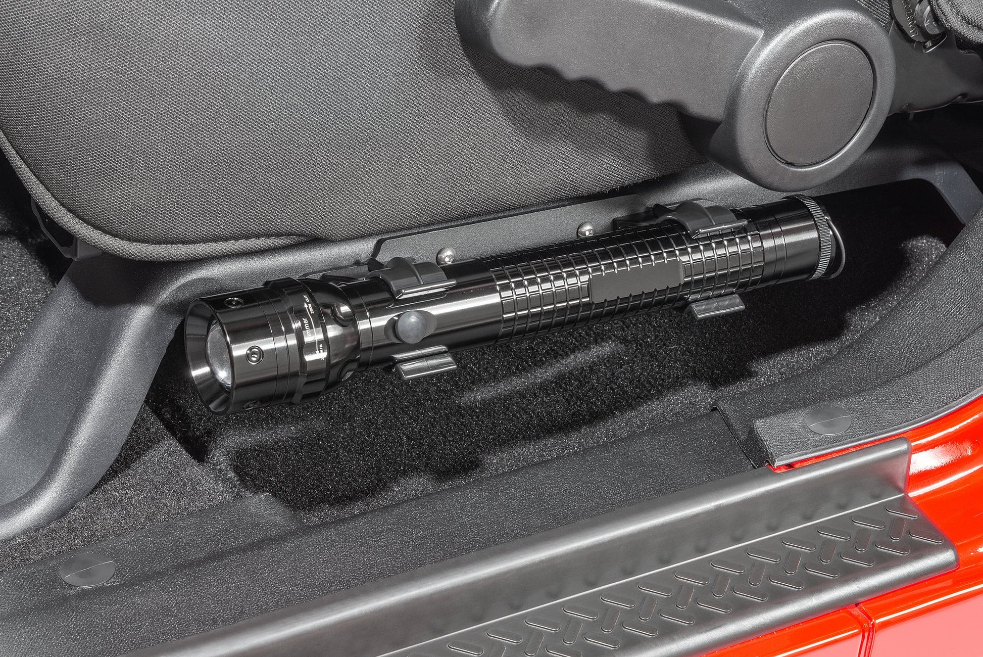 a cropped in photo of a vehicle’s driver seat with a silver metal flashlight mounted beneath