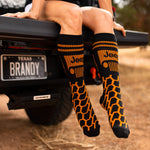 the lower half of a woman sitting on the back of a jeep wearing orange and black tread patterned socks with the jeep logo on them
